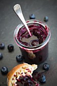 A jar of blueberry jam with a bread roll