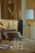 Elegant double bed with shimmering gold fabric draped over headboard next to standard lamp