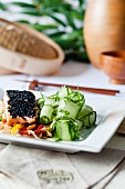 Steamed salmon with a black sesame crust on noodles, with stir-fried vegetables and fresh cucumber salad