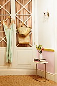 Wandschrank im 50er Jahre Stil, aufgehängtes Kleid, seitlich kleiner Beistelltisch mit Blumenvase auf Sisal Teppich in nostalgischem Ambiente