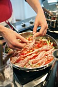 Bacon being added to a pan of fried vegetables