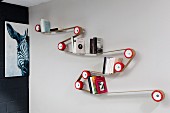 Designer bookcase made by winding strap around red rollers mounted on wall