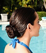 A brunette woman by a pool with her hair in a bun
