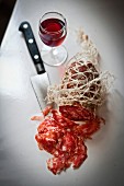 Rosette sausage in a net with a glass of red wine and a knife