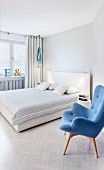 Blau bezogener Retro Sessel neben Doppelbett mit weißem Kopfende in modernem Schlafzimmer