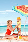 A mother applying suncream to her little daughter on the beach