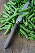 String beans with a knife on a wooden chopping board