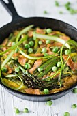 Frittata with asparagus, smoked salmon and peas in a rustic pan