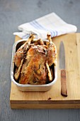 Roast chicken in a metal dish on a wooden chopping board