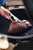 A steak with herbs being turned on a barbecue