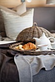 Croissant and tea on wicker tray on bed