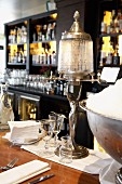 An art deco style table lamp and ice buckets behind the bar in a restaurant in front of rows of spirits and glasses