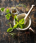 Various fresh herbs and olive oil in a mortar