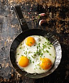Three fried eggs with chives in a hot, black pan