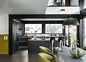 An open-plan designer kitchen in grey with a cooking island and a dining area with green, upholstered chairs in the forground
