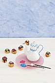 Paintbrushes, coffee pot painted with porcelain paint and cake pops with colourful decoration