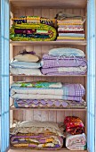 Folded bedclothes in a pastel blue laundry cupboard