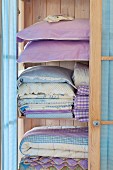 Heller Holzschrank mit gestapelter Bettwäsche und Kopfkissen in Pastelltönen