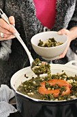 A woman ladling kale soup from a pot
