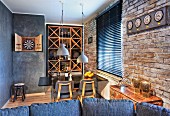View over sofa backrest to dining area with wine rack and dartboard in open-plan interior with brick wall