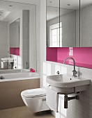Sink with towel rail below pink niche with fitted, mirrored cabinets in bathroom