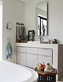 Blick über Badewanne auf gemauerten Waschtisch mit eingebautem Unterschrank in Weiß