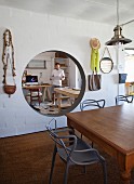 Dining table and chairs in front of round aperture in wall with view of man between two desks