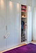 A white wardrobe with an open door and a view of clothing