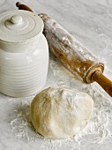 An arrangement of baking ingredients with a ball of pastry and a rolling pin