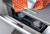 A half-opened dishwasher with a view of the control panel with a star-patterned tea towel on top
