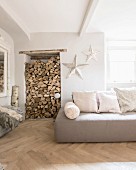 Firewood in niche next to sofa with scatter cushions and white patinated stars on wall