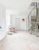 Vintage spiral staircase in open-plan interior with herringbone parquet floor and armchair next to window