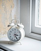 White, retro-style alarm clock on windowsill and wall with vintage patina