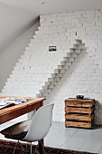 Wooden table and classic chair in front of rustic console table made from wooden crates in whitewashed brick niche