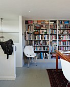 Classic shell chair with white fur blanket against bookcase in simple interior
