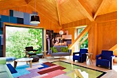 Holzvertäfelter Wohnraum in zeitgenössischer Architektur, Patchworkteppich auf verglastem Bodenbereich, blaue Sessel