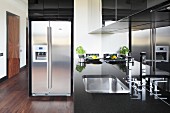 Black kitchen counter with stainless steel sink, glossy splashback and stainless steel fridge-freezer combination