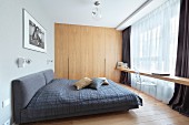 Dunkelgraues Doppelbett und zwischen Wänden eingespannte Holztischplatte vor dem Fenster, Einbauschrank aus Holz im Schlafzimmer