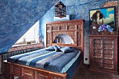 Bed with carved wooden frame and Oriental-style headboard in attic room with mottled blue walls