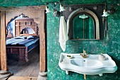 Sink on green, sponged wall next to open door with carved wooden frame and view into bedroom