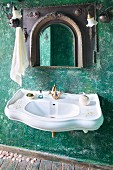 Geschwungener Waschtisch mit Vintage Messingarmatur und Spiegel mit orientalisch geformtem Rahmen an grüner Wand