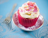 A vanilla cupcake decorated with pink sugar and fondant flowers