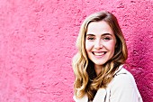 A portrait of a dark blonde woman against a pink wall