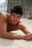 A young, topless man lying in the sand