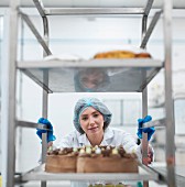 Bäckerin schiebt Rollwagen mit frisch gebackenen Kuchen in der Kuchenfabrik