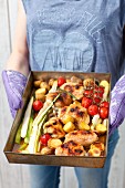 A woman serving roast chicken bits with asparagus, cherry tomatoes and potatoes
