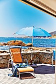 Liegestuhl mit Badetuch und Sonnenschirm auf Terrasse am Meer