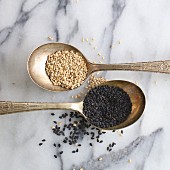 Light and dark sesame seeds on silver spoons (close-up)