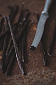 Vanilla pods and a knife with scrapped out seeds on the tip of a knife