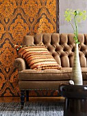 African ceramic vase on stool, ethnic scatter cushion on antique sofa and wallpaper with majestic pattern